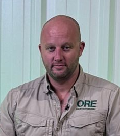 A person with a shaved head wearing a tan collared shirt with an