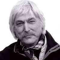 A black-and-white portrait of a person with long hair and a mustache, wearing a scarf and jacket.