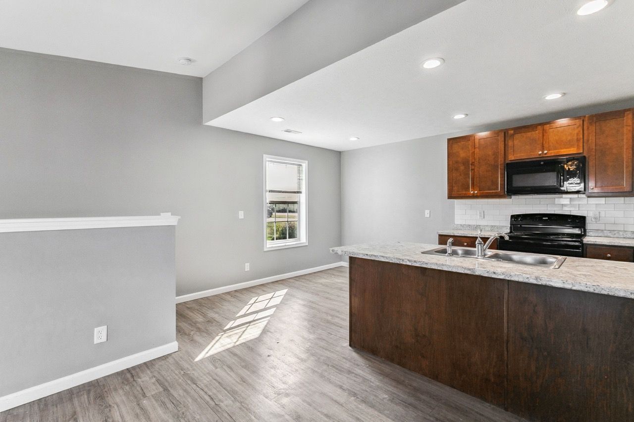 Open-concept kitchen with brown cabinets, gray walls, and a large island. Sunlight streams in from a window.