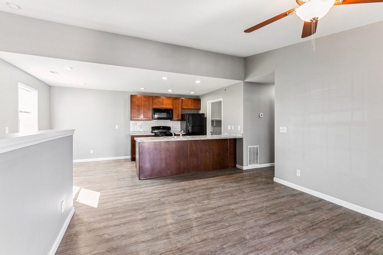 Open-concept living space with kitchen. Wooden cabinets and island, gray walls, and wood-look flooring.