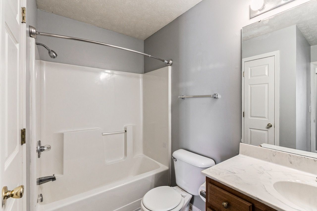 Bathroom with a white bathtub, toilet, and vanity against gray walls.