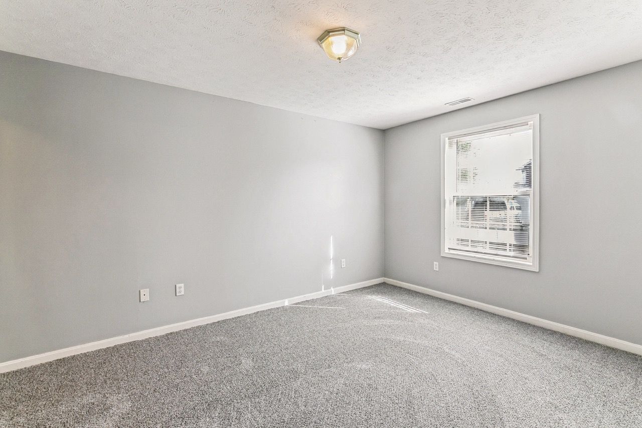 Empty room with gray walls, carpet, and a window.