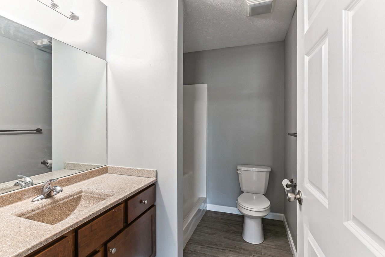 Bathroom with brown vanity, toilet, and shower. Gray walls, white door.