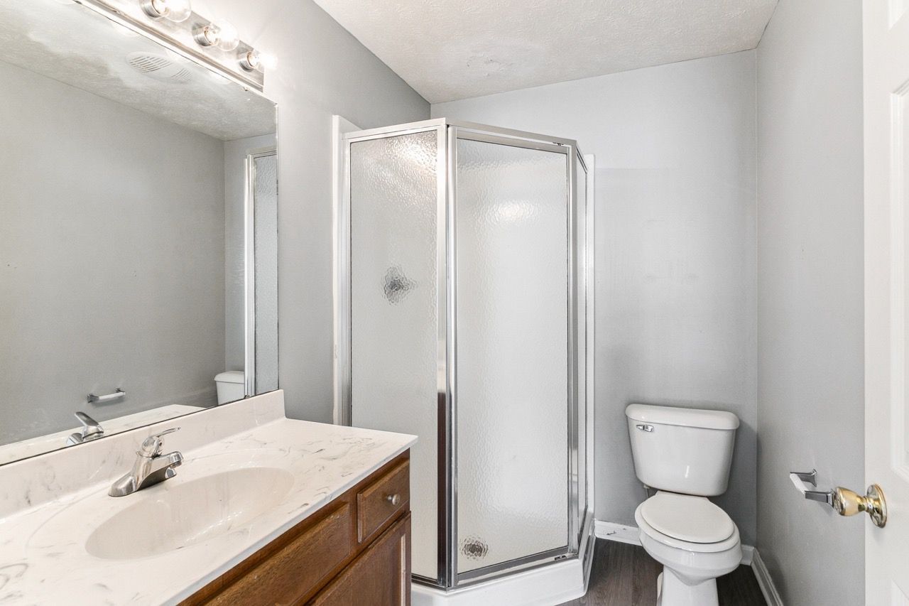 Bathroom with a shower, toilet, and vanity against gray walls.