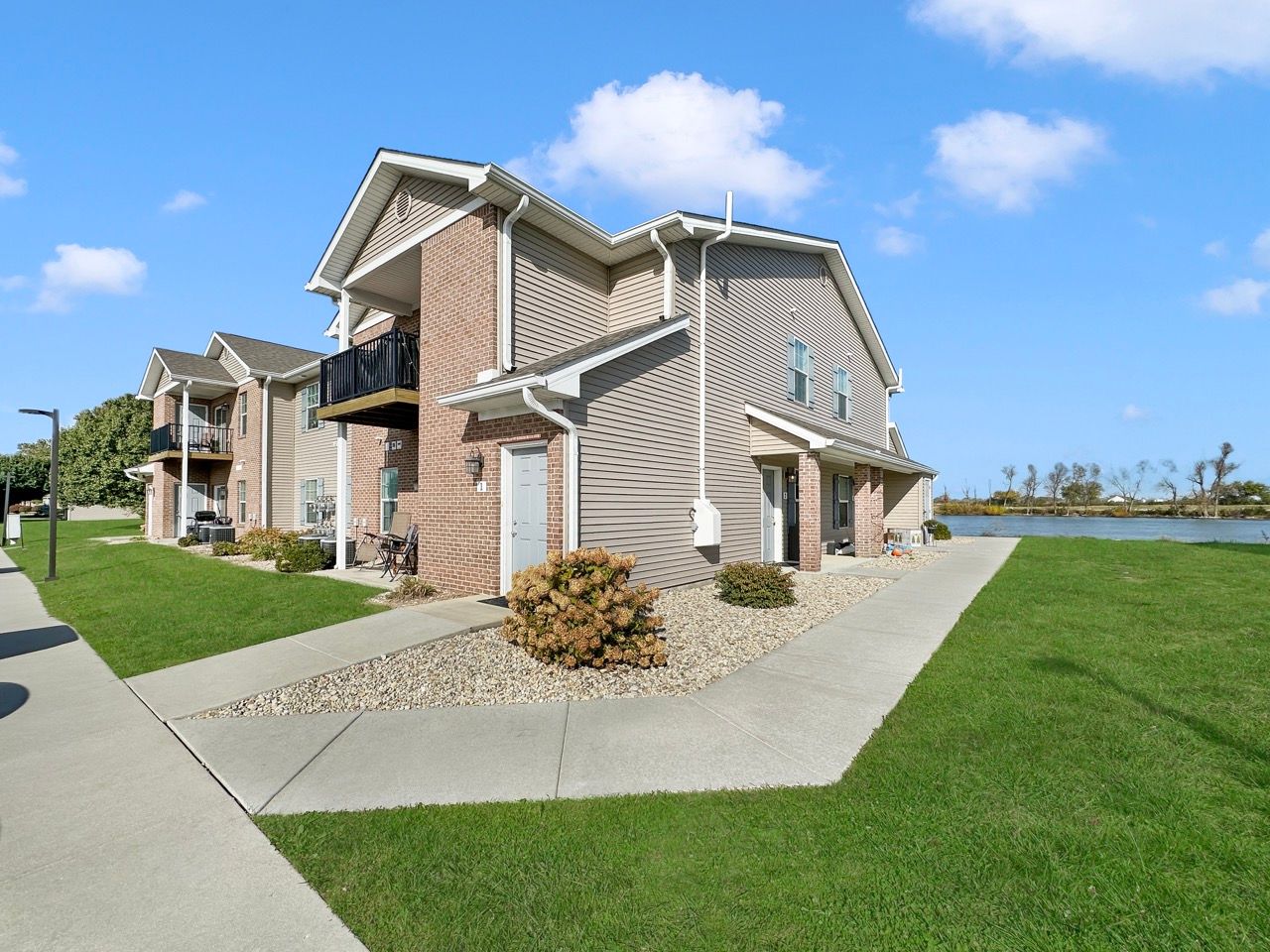 Multi-unit residential building with beige siding, brick accents, and a balcony on a sunny day.