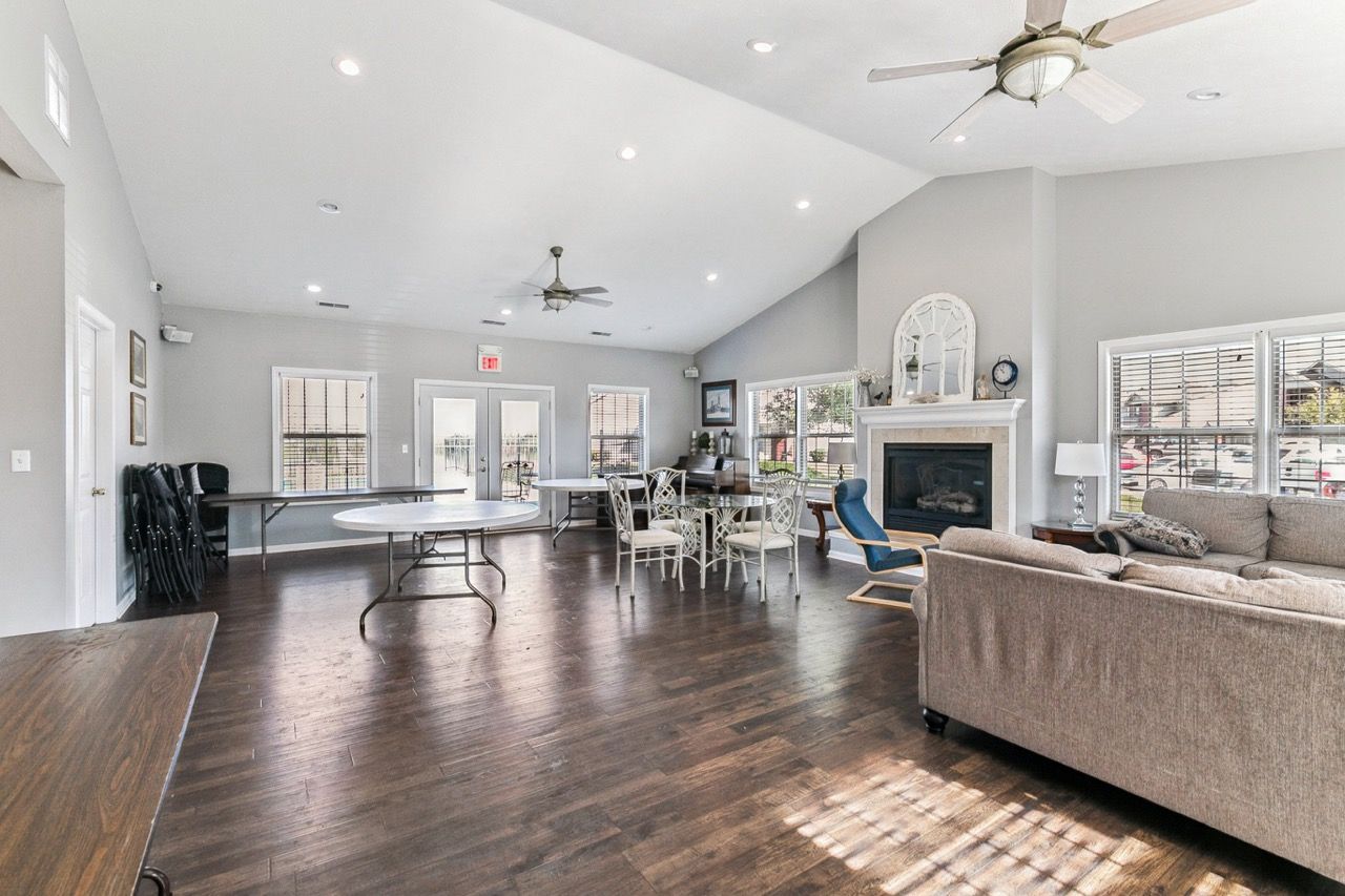 Spacious community room with fireplace, round tables, chairs, and a large sofa; hardwood floors.