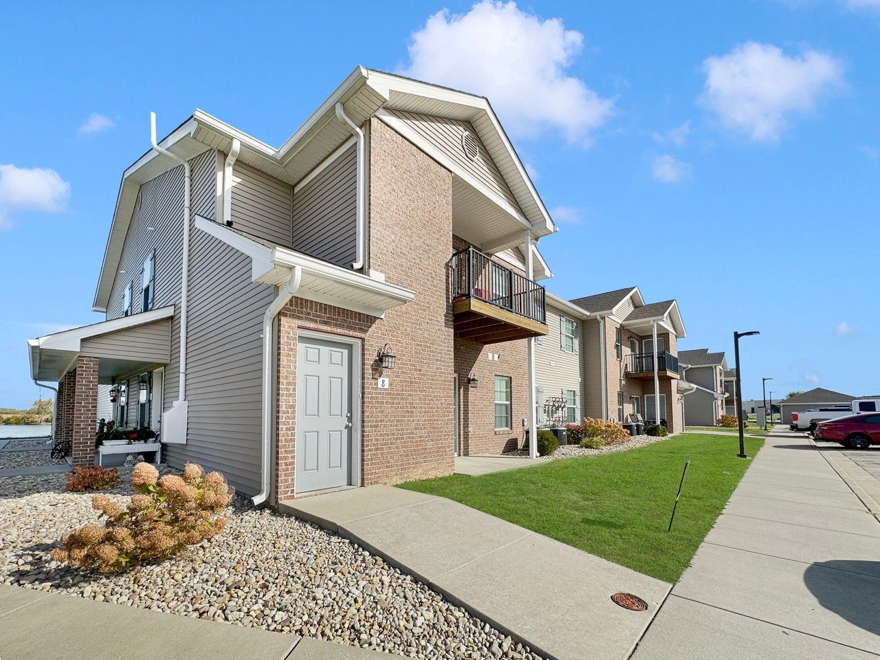 Two-story apartment building with brick and beige siding, a walkway, and blue sky.