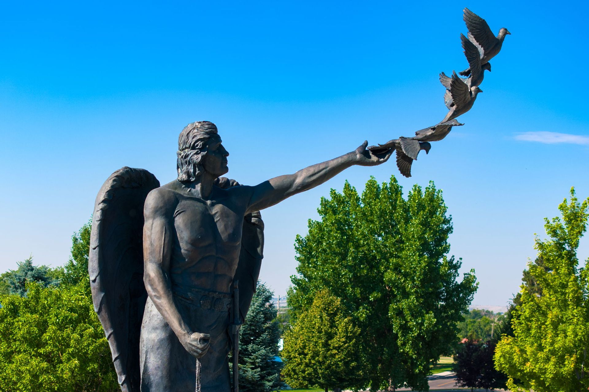 A statue of a man with wings holding a bunch of pigeons