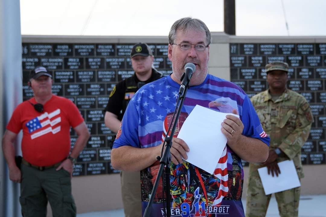 A man in an american flag shirt is speaking into a microphone