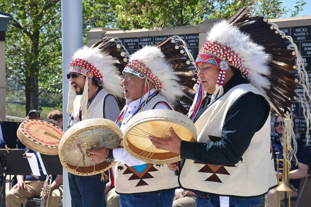A group of men in native american costumes are playing drums.