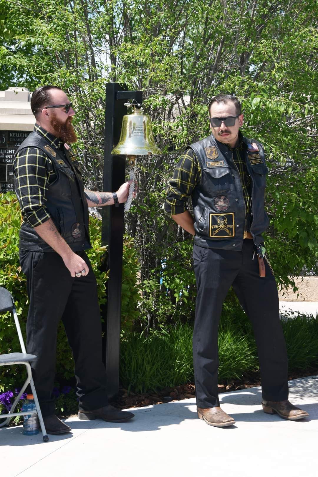 Two men are standing next to each other in front of a bell.