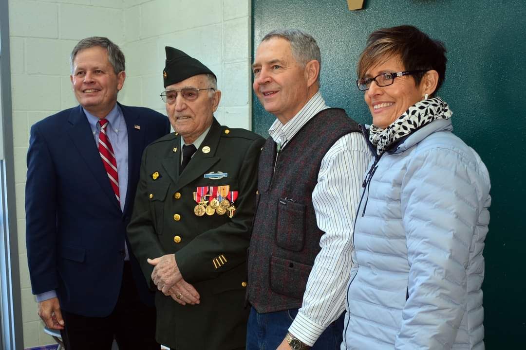 A man in a military uniform is standing next to two other men and a woman.
