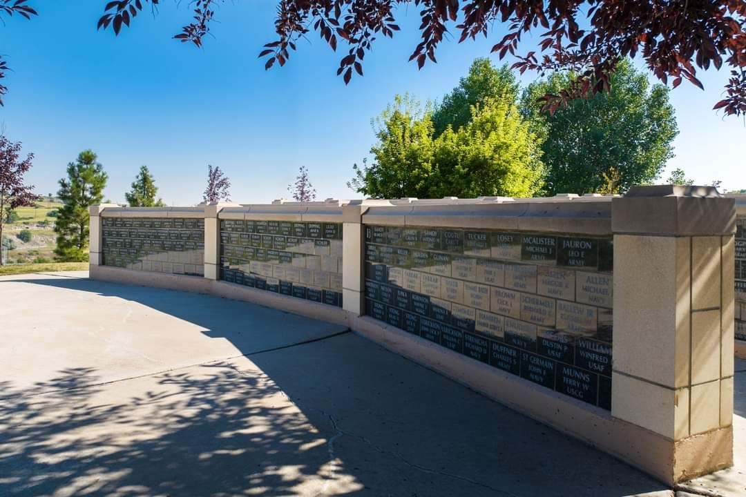 A stone wall with a plaque on it in a park with trees in the background.