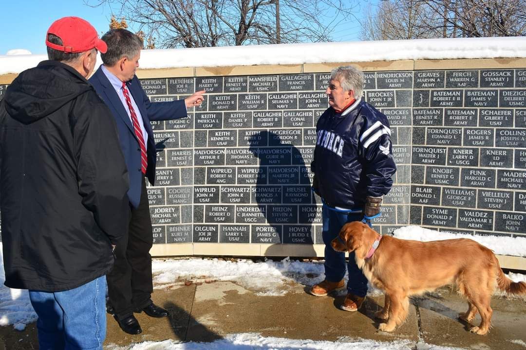 Three men and a dog are standing in front of a brick wall