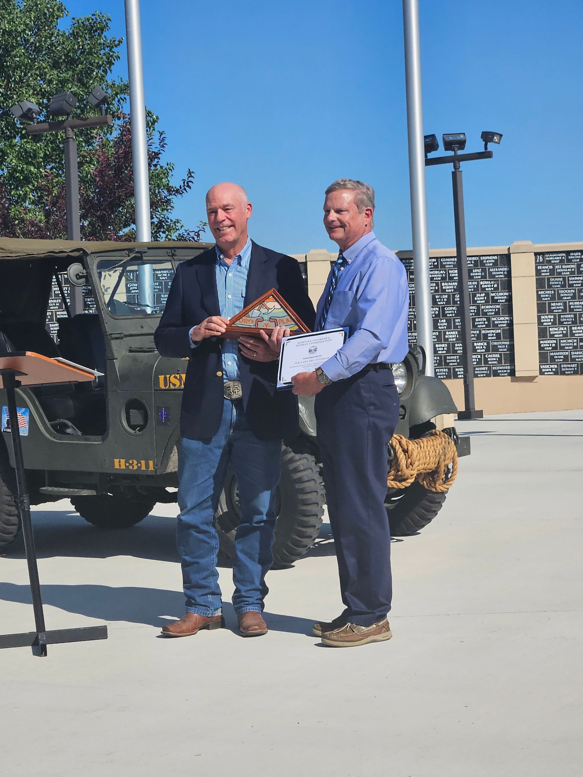 Two men are standing next to each other in front of a jeep.