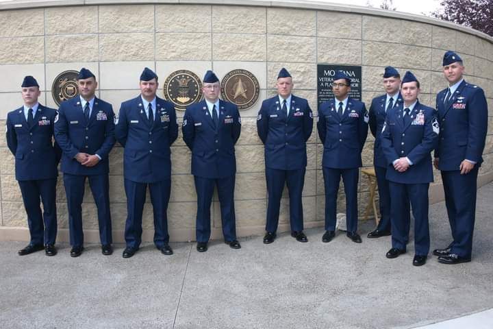 A group of men in military uniforms stand in front of a brick wall