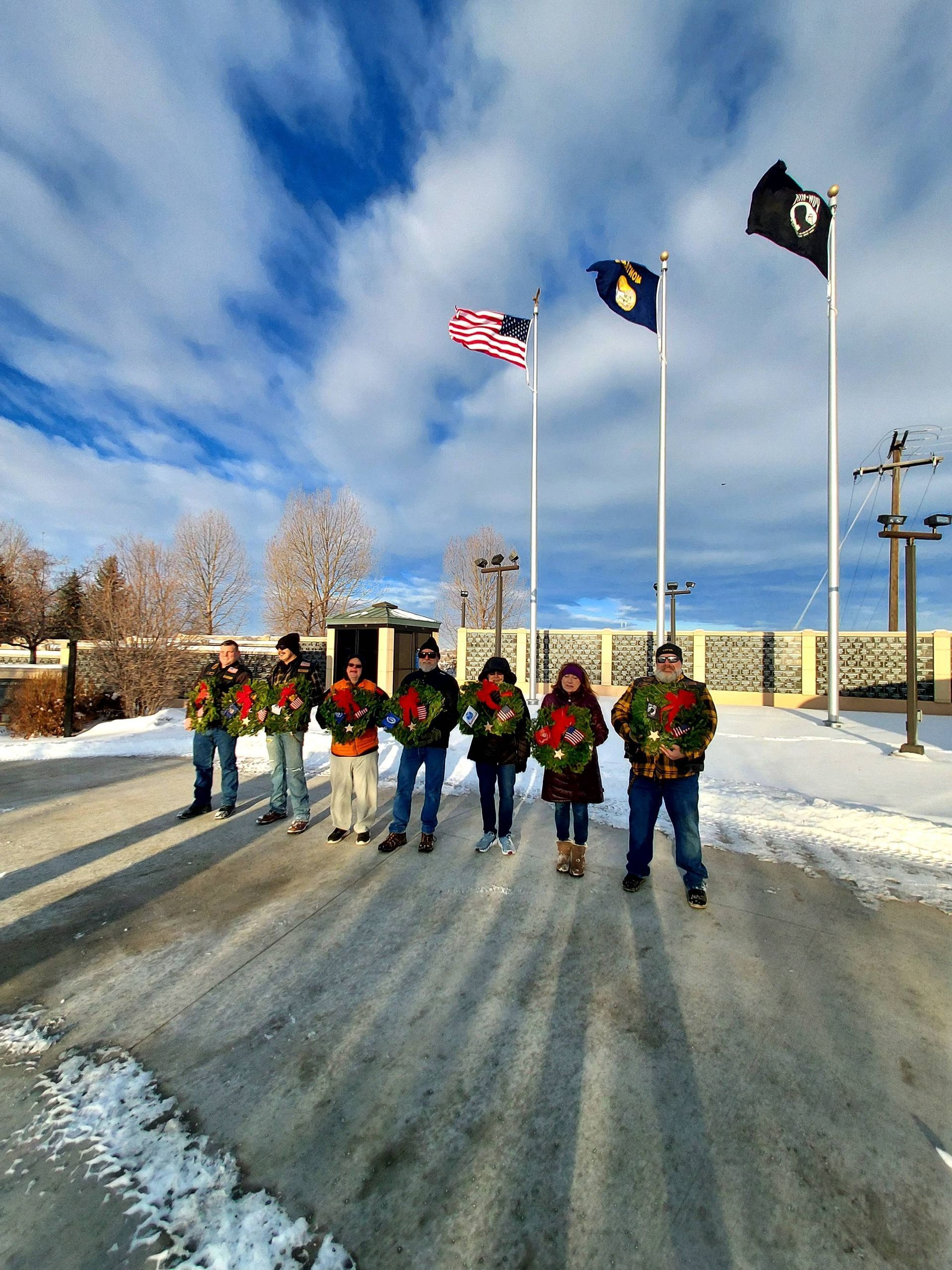 A group of people standing in the snow holding wreaths in front of flags.