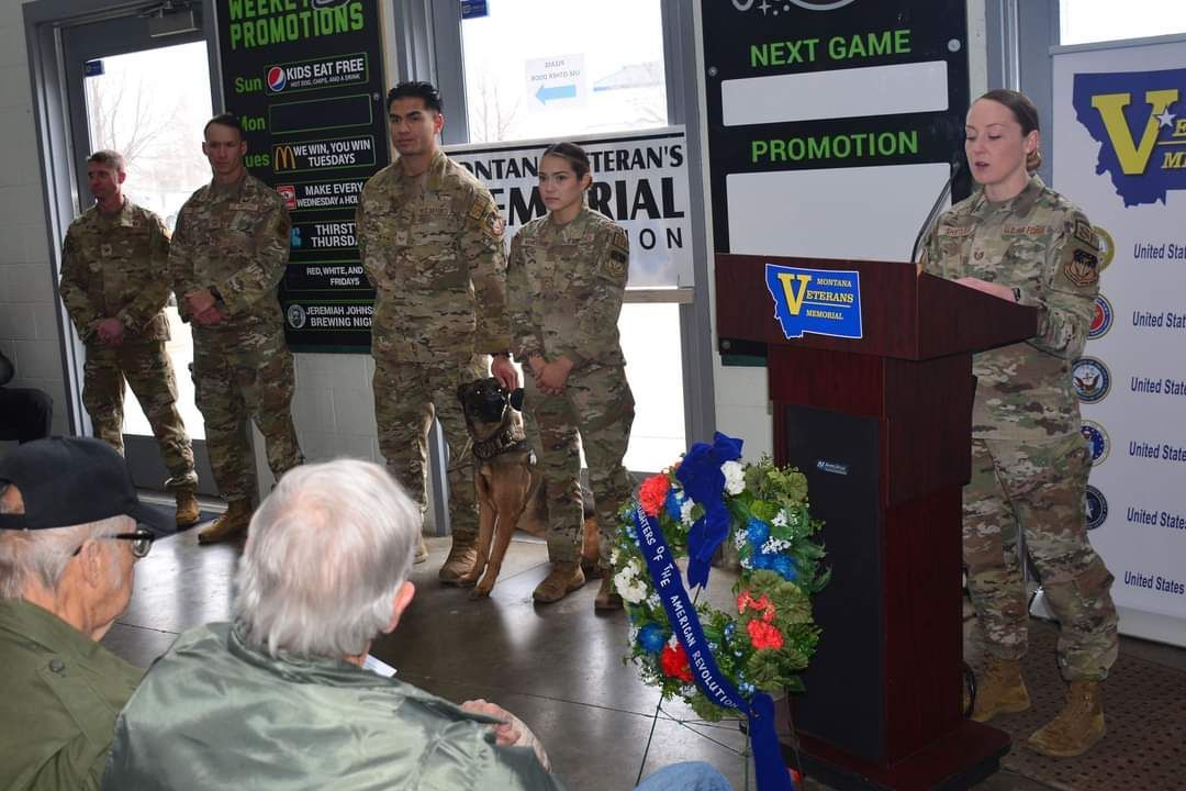 A group of soldiers are standing around a podium with a wreath in front of them.
