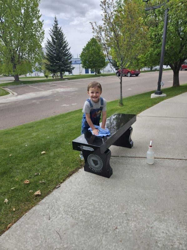 A little boy is sitting on a bench cleaning it.