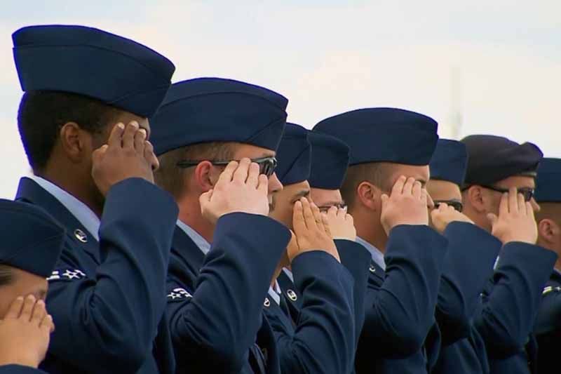 A group of soldiers saluting in a line with their hands on their faces.