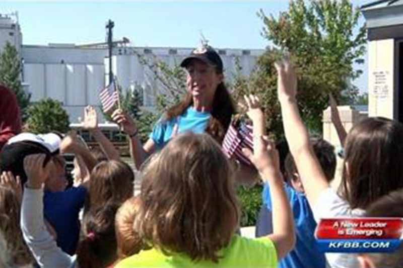 A woman is standing in front of a group of children holding american flags.