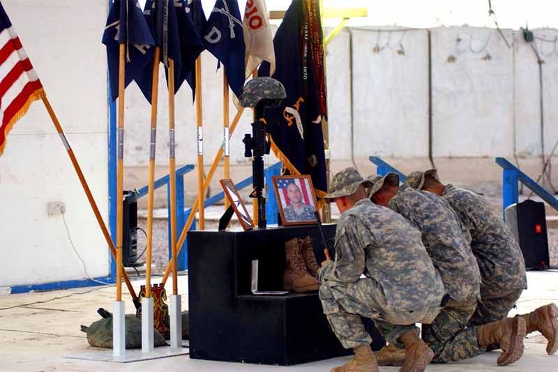 A group of soldiers are kneeling down in front of a memorial