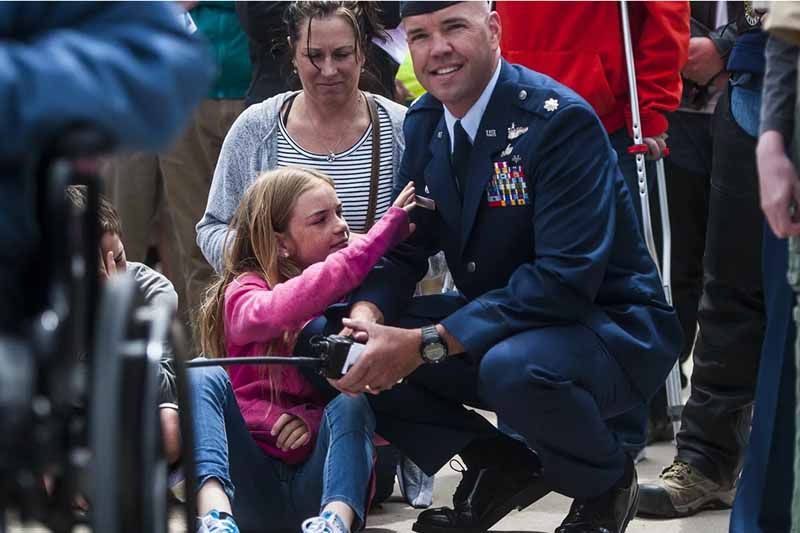 A man in a military uniform is kneeling down with a little girl