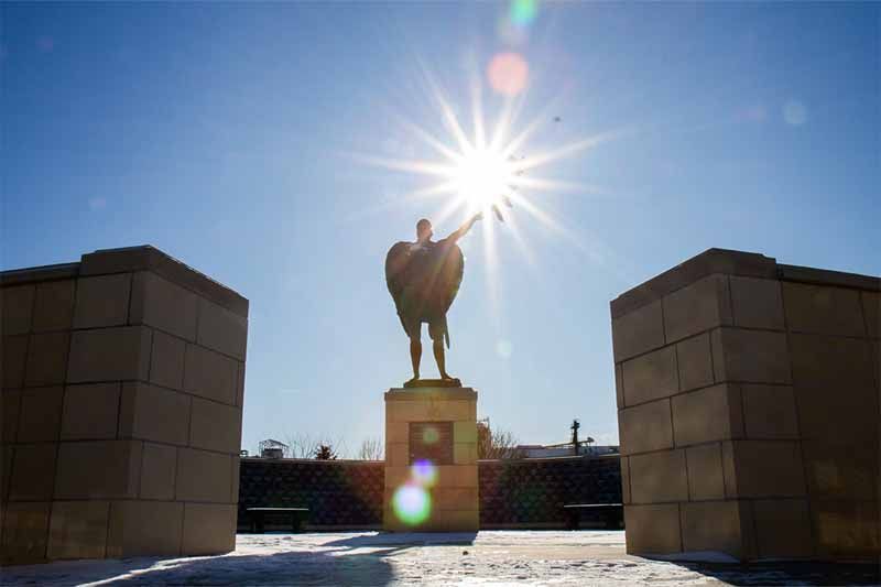 A statue of a man with wings in front of the sun