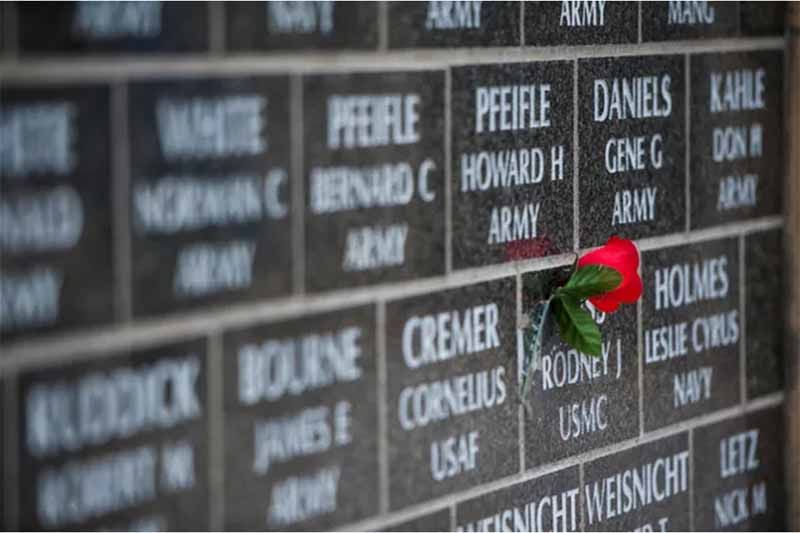 A red rose is sitting on top of a memorial wall.