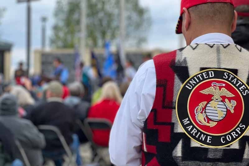 A man wearing a united states marine corps vest is standing in front of a crowd of people.