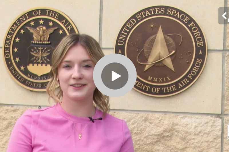 A woman in a pink shirt is standing in front of a united states space force sign