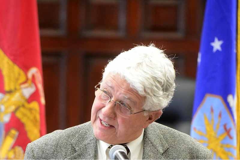 A man in a suit and tie is smiling in front of two flags