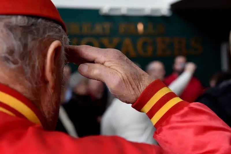 A man in a red and yellow jacket salutes in front of a crowd.