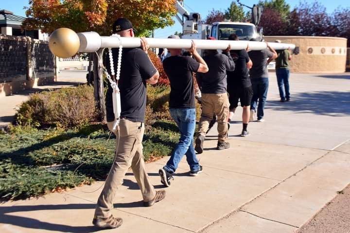 A group of men are carrying a large pole down a sidewalk