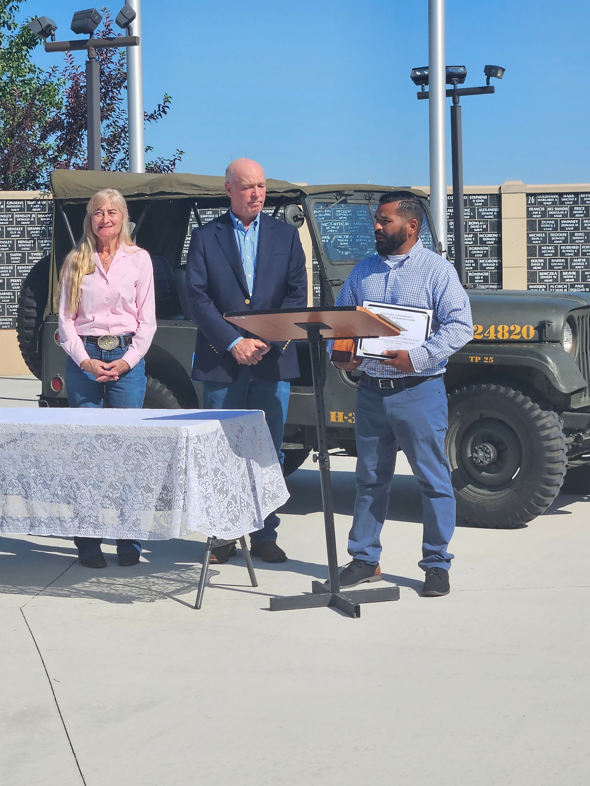 A man stands at a podium with a jeep in the background