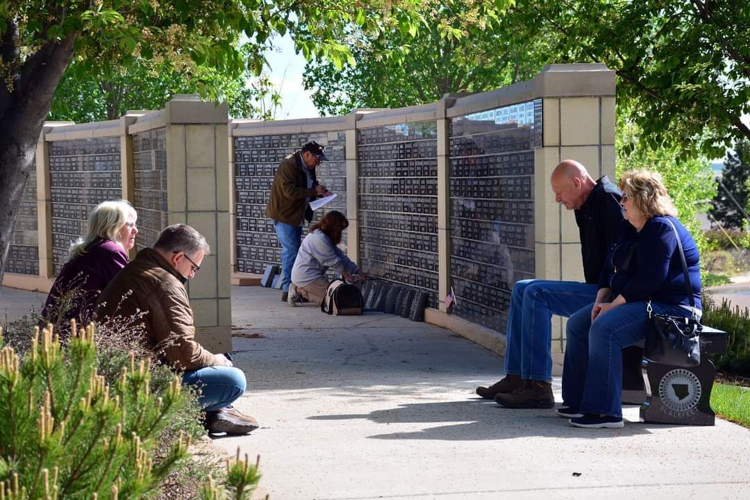 A group of people are sitting on a sidewalk in front of a wall.