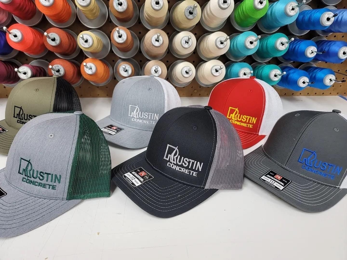 Trucker hats with embroidered logos in front of spools of thread.