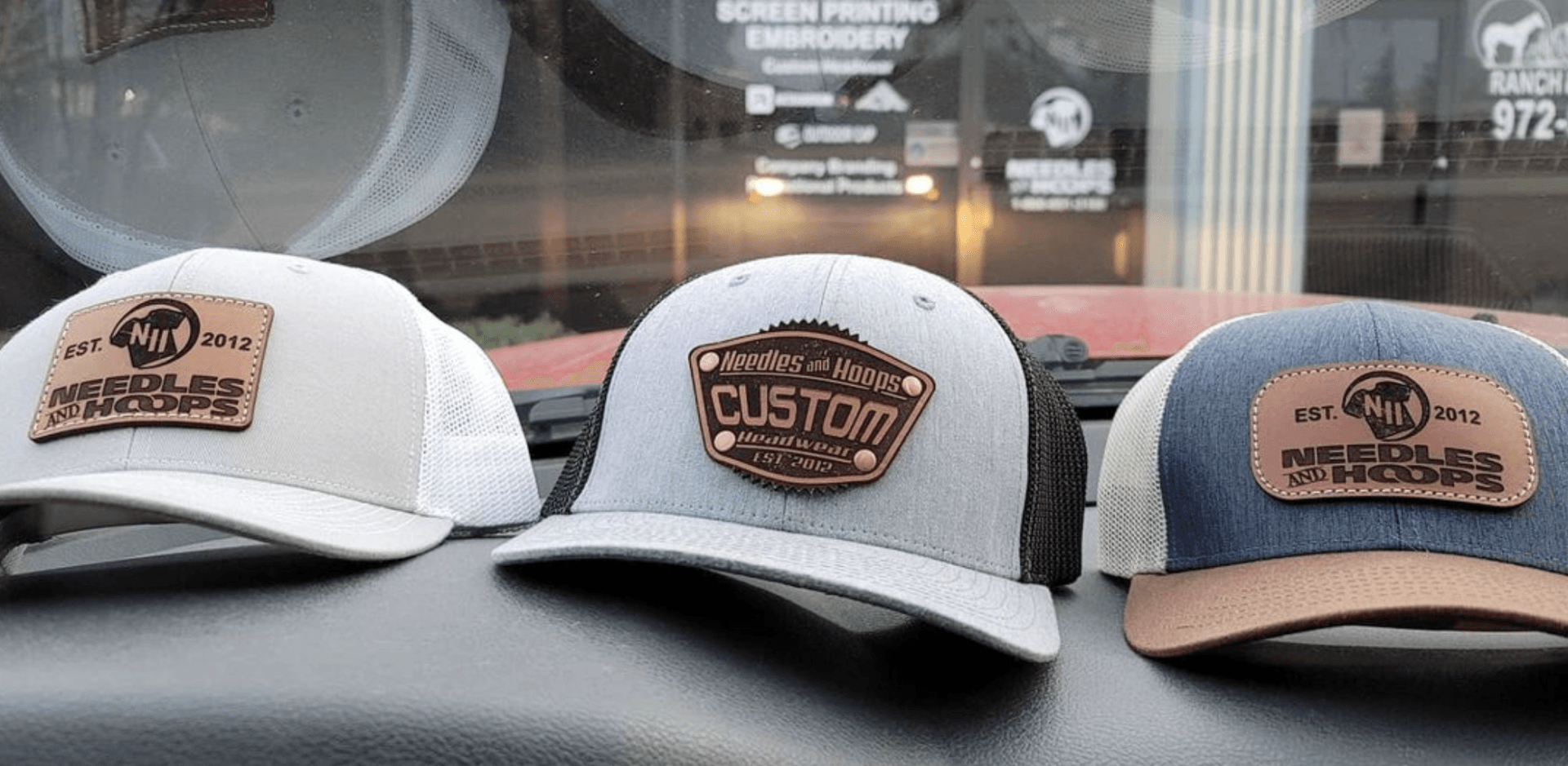 Three trucker hats with custom leather patches, various colors, displayed on a dashboard.