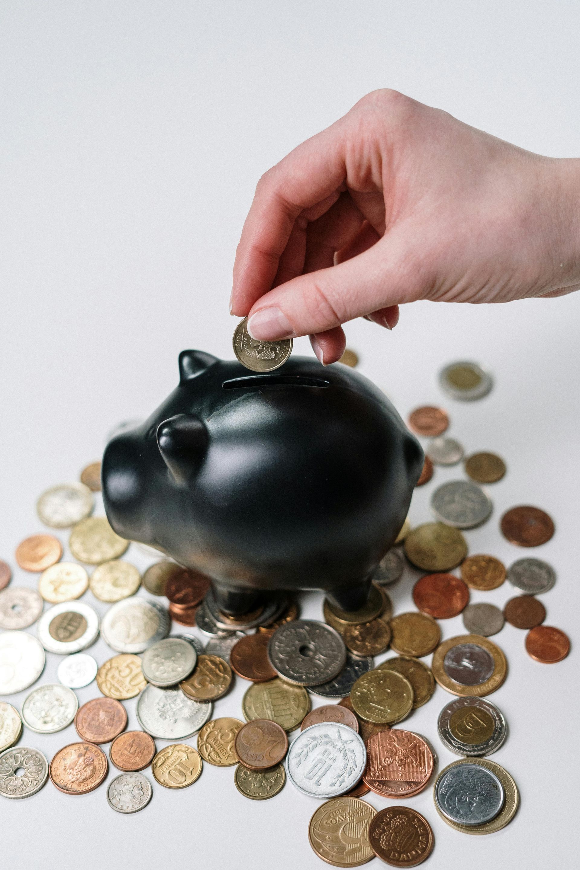 A person is putting a coin into a piggy bank surrounded by coins.