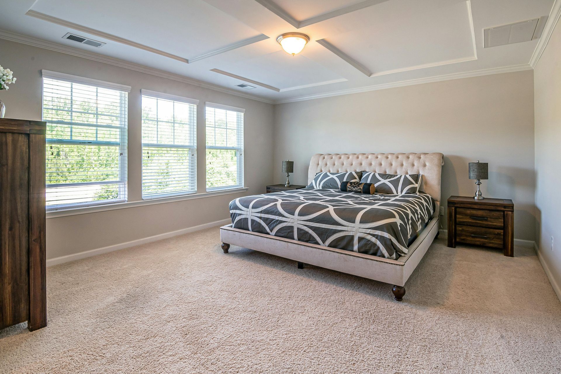 A bedroom with a large bed , two nightstands , a dresser and two windows.