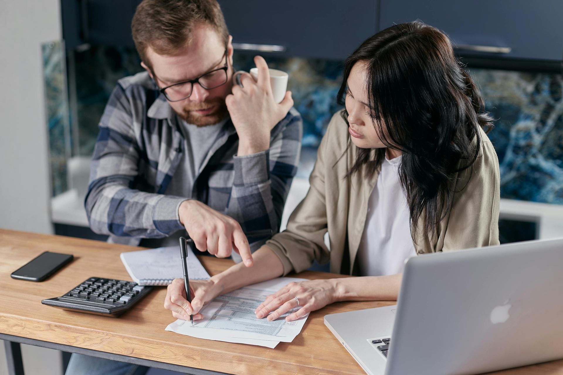 A man and a woman are sitting at a table looking at papers and a laptop.