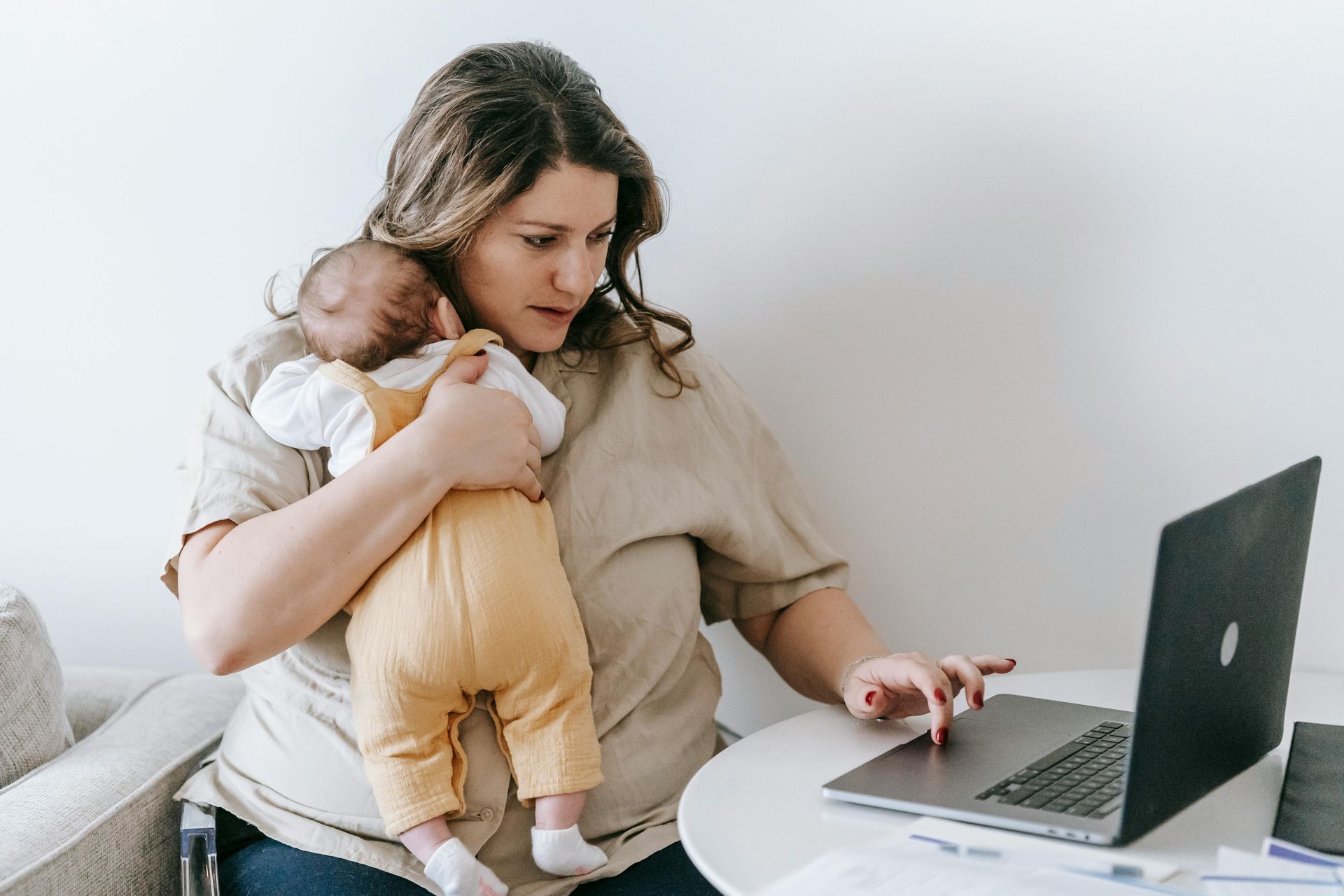 A woman is holding a baby while using a laptop computer.