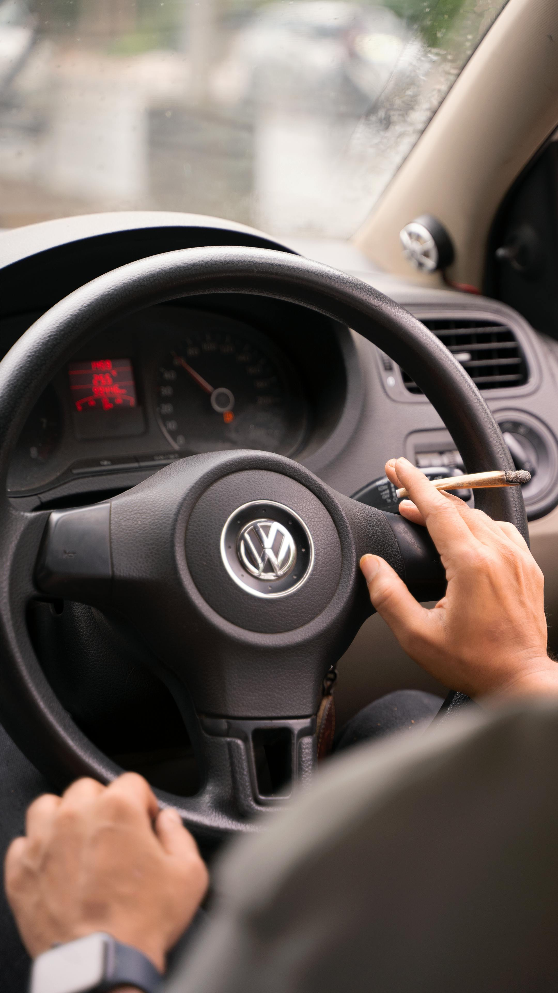 Driver’s hands on a Volkswagen steering wheel, holding a phone while driving inside a car