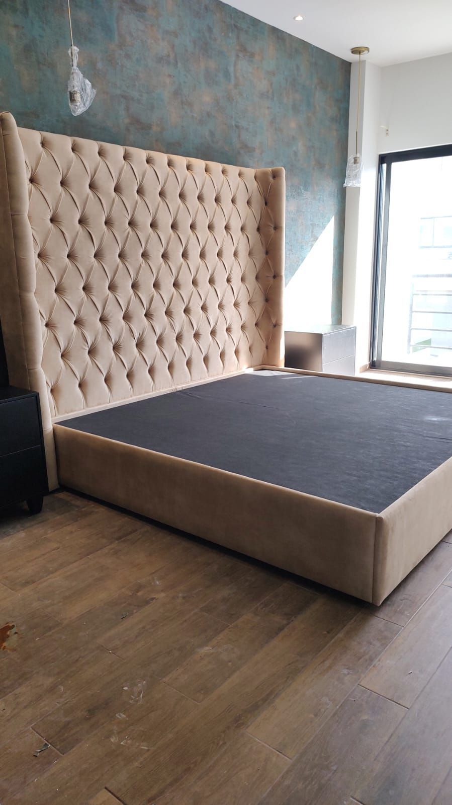 Una cama con cabecera capitoné se encuentra sobre un piso de madera en un dormitorio.