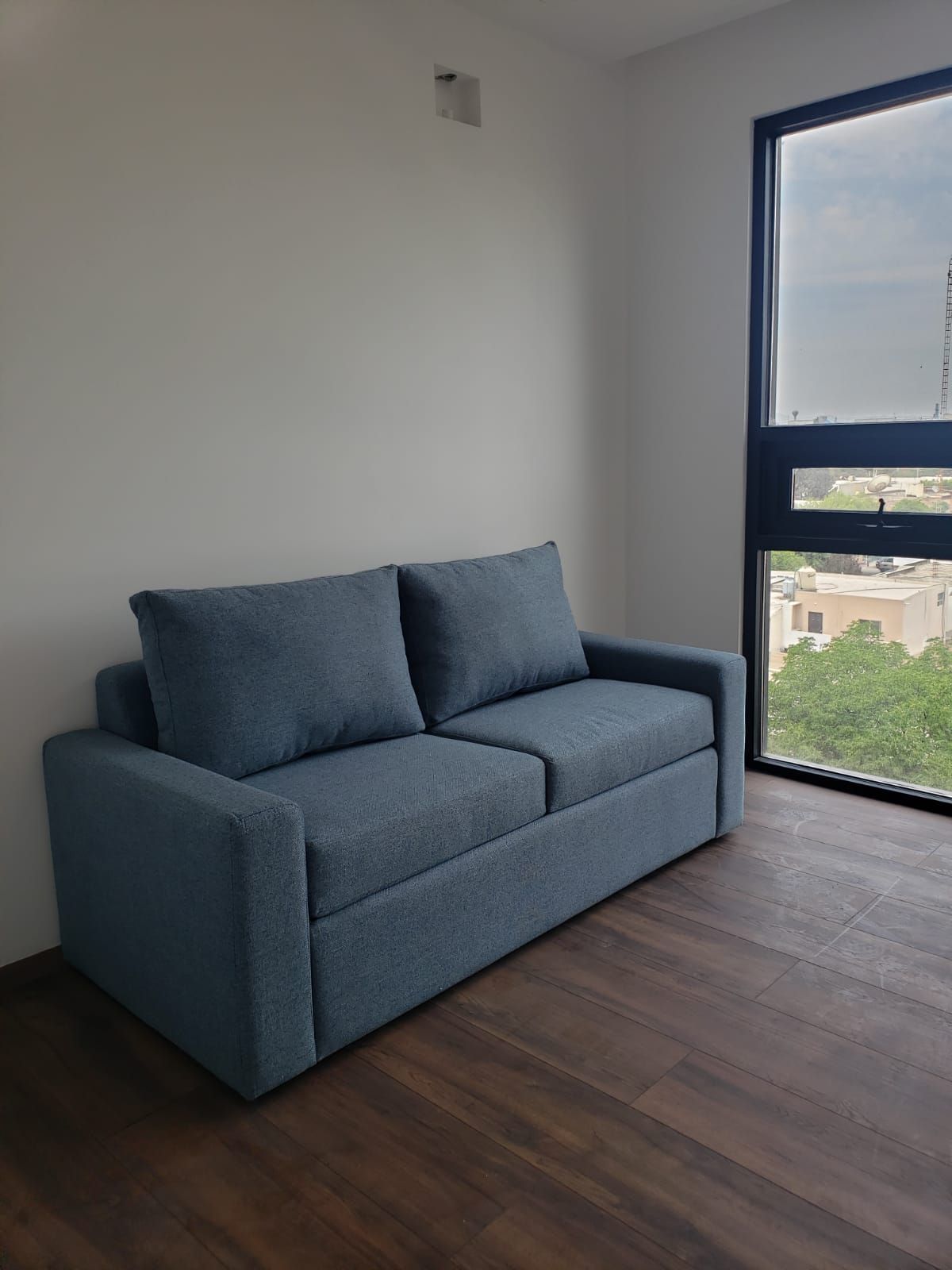 Un sofá azul está en una habitación al lado de una ventana.