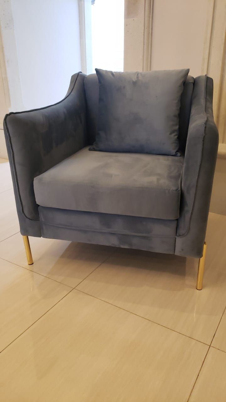 Una silla gris con patas doradas reposa sobre un suelo de baldosas.