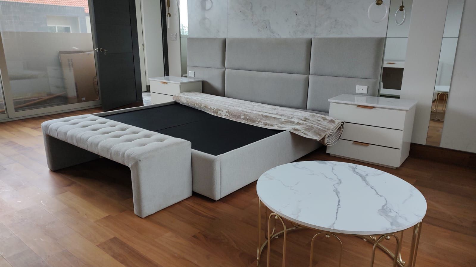 Un dormitorio con una cama, una otomana, una mesita de noche y una mesa de café.