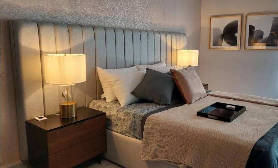 Un dormitorio con cama, mesita de noche, lámparas y cuadros en la pared.