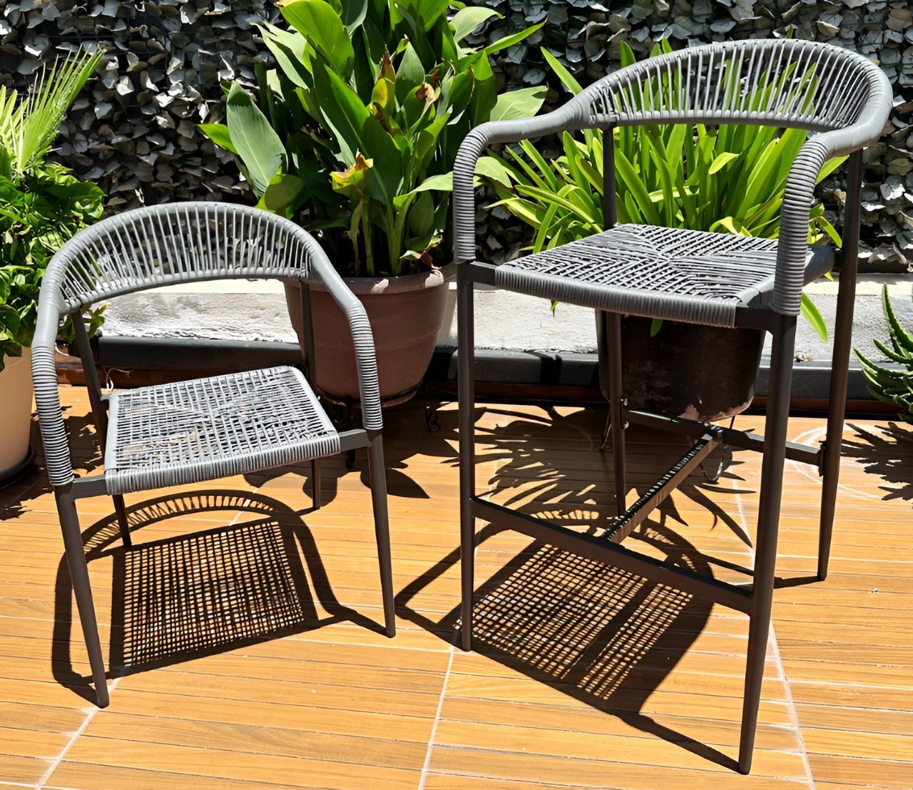 Dos sillas de mimbre están colocadas sobre un suelo de baldosas frente a plantas en macetas.