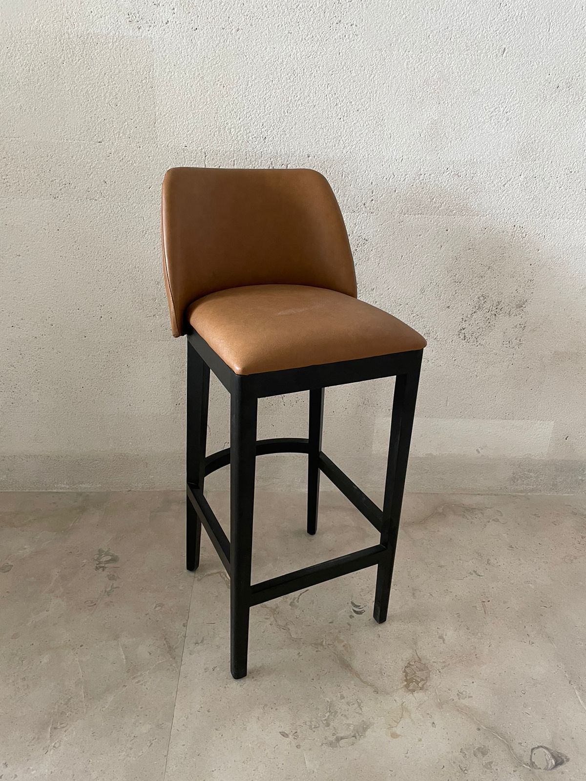 Un taburete de bar marrón con marco negro está sobre un suelo de baldosas.
